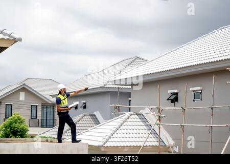 African American civil engineer holding walkie talkie and clipboard inspecting residential building site during daytime, scene for housing development Stock Photo