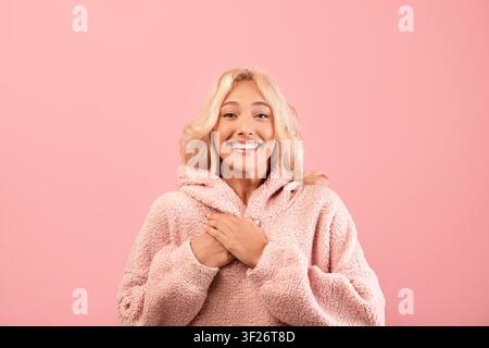 Smiling Young Woman In Pink Fuzzy Hoodie Against Pink Background, Joyful Emotion Stock Photo