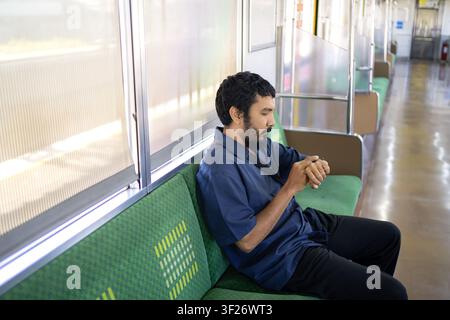 Indonesian commuter checking smartwatch while seated inside a train carriage. Public transportation, time management and daily travel concept. Stock Photo