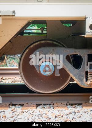 Close up side view of a rusted railway freight car wheel assembly showing the mechanical axle bearing cap on steel tracks Stock Photo