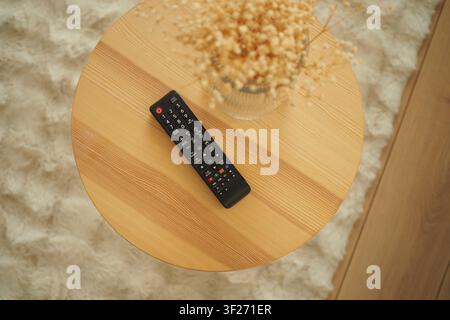 Remote control sits on a wooden table with some decoration Stock Photo
