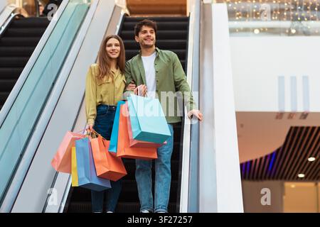 Happy Young Couple Holding Colorful Shopping Bags At Shopping Mall, Shopping Concept Stock Photo