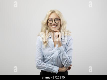Smiling Young Caucasian Woman In Blue Shirt Holding Hand On Chin, Business Concept Stock Photo