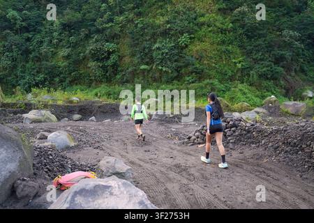 Two hikers walking side by side on a rocky trail surrounded by lush forest, wearing sporty outdoor gear. Stock Photo