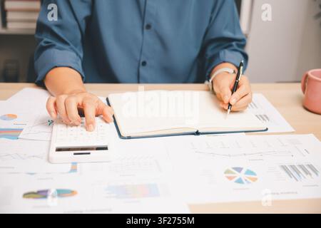 Accountant using calculator and notebook on financial charts in a bright office, showing budget planning, business analysis, report review, accounting Stock Photo
