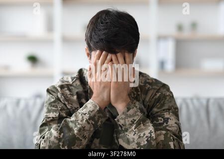 Worried Young Middle Eastern Man In Military Uniform Covering Face With Hands, Home Setting Stock Photo