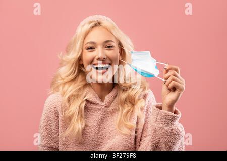 Smiling Young Woman Holding Face Mask And Laughing, Pink Background, Healthcare Concept Stock Photo