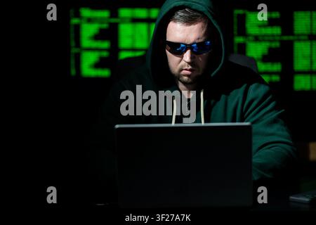 Cybersecurity hacker works on laptop. Cybersecurity hacker analyzes green code. Cybersecurity hacker monitors network threat. Cybersecurity hacker Stock Photo