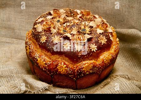 A loaf of bread with decorations on the background of burlap. A close-up of the festive loaf. Stock Photo