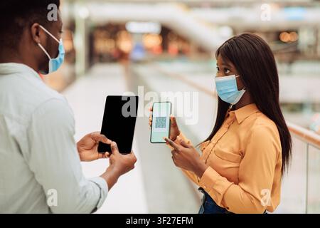 Focused Black Woman Showing Qr Code On Smartphone To Man At Shopping Mall, Business Concept Stock Photo