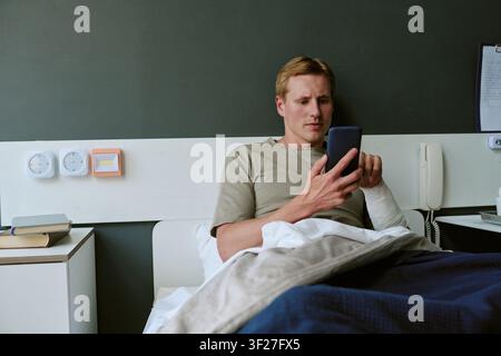 Young Adult Man Recovering in Military Hospital While Using Smartphone Stock Photo
