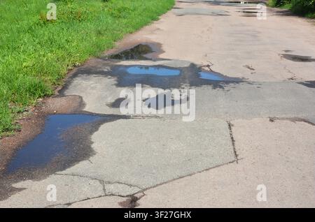 Asphalt  on puddles. Pot hole or pothole image of a broken cracked asphalt pavement with a dirty water puddle as a transportation symbol of road maint Stock Photo