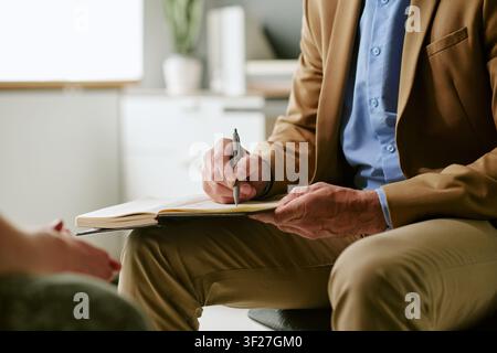 Male Therapist Taking Notes during Mental Health Counseling Session Stock Photo