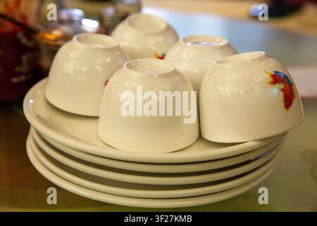 A group of small, upside-down white ceramic Chinese tea cups decorated with colorful koi fish patterns, stacked neatly on matching porcelain plates. Stock Photo