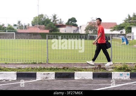 Asian Indonesian young man walking beside sports field carrying training bag, representing active lifestyle, exercise routine, and healthy movement. Stock Photo