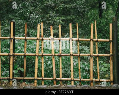 Traditional bamboo fence with black rope lashings in a rain-soaked forest at Meiji Shrine, Shibuya, Tokyo, Japan Stock Photo