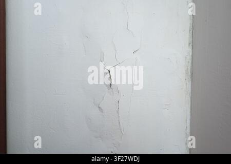 A close up of a spider web crack pattern on a white interior wall, featuring peeling paint and plaster damage, which indicates potential moisture issu Stock Photo