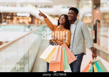 Happy Young African American Couple Shopping Together At Mall, Holding Colorful Bags Stock Photo