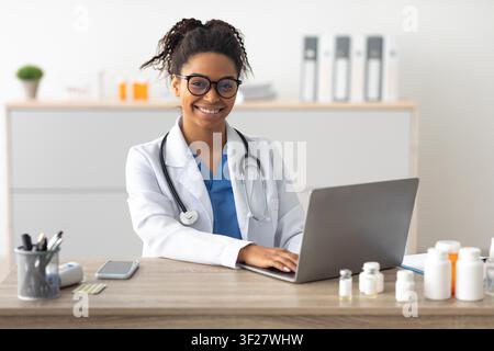 Smiling Black Female Doctor Working On Laptop In Healthcare Office Setting Stock Photo