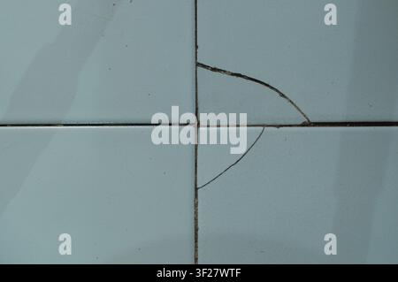 Detailed texture of cracked and chipped ceramic floor tiles with stained grout, showing age, damage, and wear in a bathroom or kitchen. Stock Photo