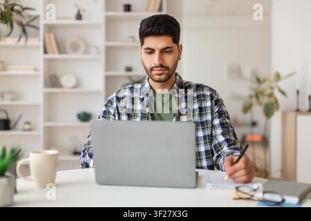 Focused South Asian Male Working On Laptop In Modern Home Office, Remote Work Concept Stock Photo