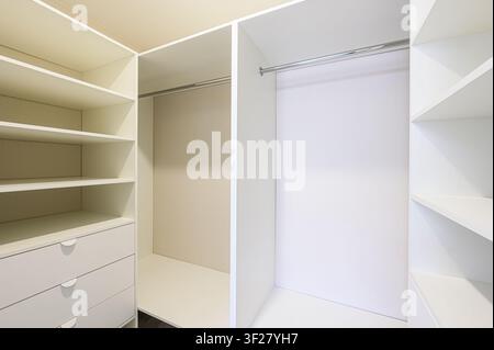 clean, modern, walk-in closet interior. It features white shelves, drawers, and hanging rods, with empty spaces, suggesting organization and storage Stock Photo