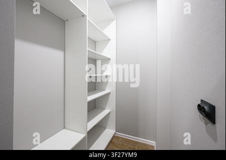 minimalist interior shot of an empty walk-in closet with white shelving. A modern outlet is on the textured wall Stock Photo