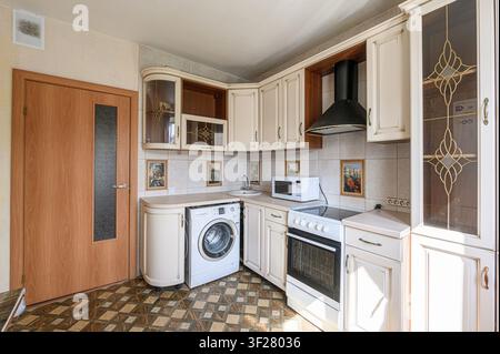 Cozy kitchen with classic cabinets, appliances (stove, microwave, washing machine), and patterned flooring Stock Photo