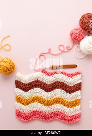 Colorful crochet project with yarn balls and crochet hook on pastel pink background. DIY crochet project with colorful wool and hook, flat lay. Stock Photo