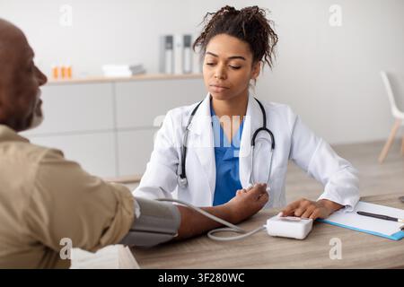African American Female Nurse Checking Blood Pressure Of Senior Male Patient In Clinic, Healthcare Concept Stock Photo