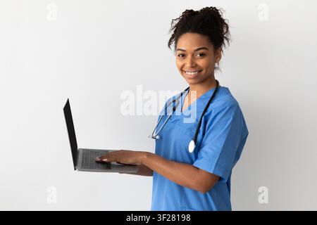 Smiling Black Female Healthcare Worker Using Laptop In Clinic, Healthcare Concept Stock Photo