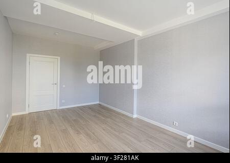 Empty room with light gray walls, wood flooring, and a white door. Clean and simple interior design Stock Photo