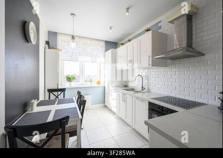 Modern kitchen with dark cabinets, stone backsplash, a stainless steel microwave, and built-in lighting Stock Photo