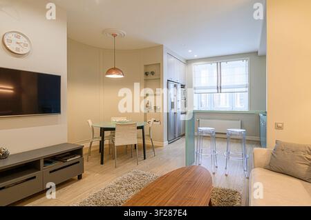 modern apartment interior featuring a living area with a TV, dining table, and a kitchen area with bar stools, all in neutral tones with pops of color Stock Photo