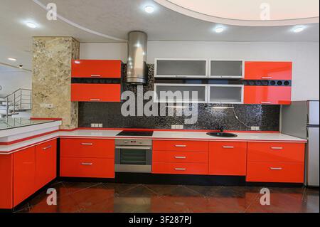 modern kitchen with red cabinets, black backsplash, and shiny floor. The kitchen has modern appliances, a stainless steel vent hood, and gray upper ca Stock Photo