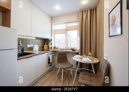 cozy kitchen with white cabinets, wooden accents, a dining table set for two, and natural light Stock Photo