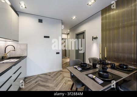 modern kitchen and dining area. Grey cabinets, marble backsplash, black hardware, and a set table with black dishes. Gold accents are visible Stock Photo