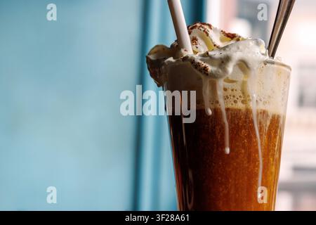 Close up of irish coffee topped with whipped cream and cocoa powder, served in a tall glass with a straw and spoon. Stock Photo