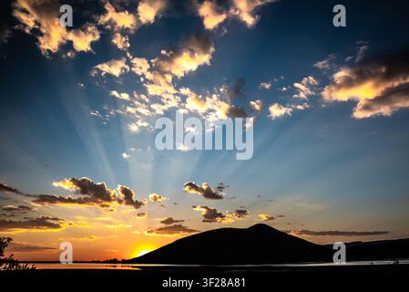 Sunlight beams from behind a silhouetted hill at sunset Stock Photo