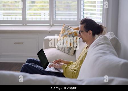 Man Typing on Laptop While Sitting on Living Room Couch Stock Photo