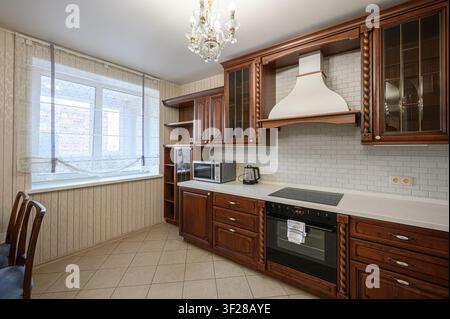 kitchen featuring dark wood cabinetry, white countertops, and a classic chandelier. A window with sheer curtains provides natural light Stock Photo