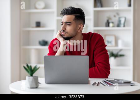 Pensive Young Asian Man Thinking At Home Office Desk With Laptop, Business Concept Stock Photo