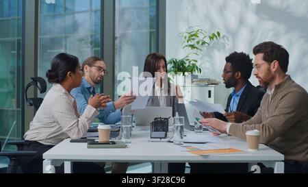 Multicultural business team working with paperwork sharing documents with financial marketing results stats at office meeting. Multiethnic colleagues Stock Photo