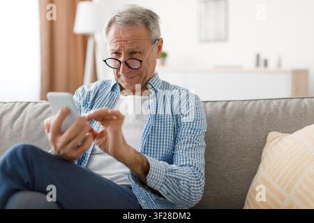 Worried Elderly Caucasian Man Using Smartphone At Home, Healthcare Concept Stock Photo