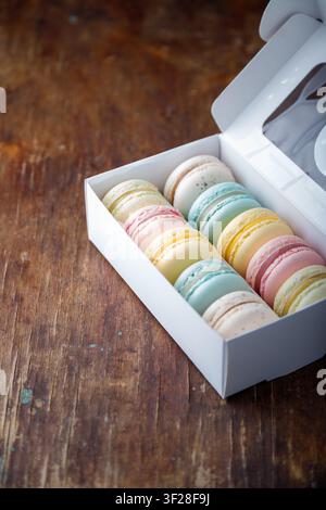 Multicolored macaroons in white box on old wooden background. Copy space. Stock Photo