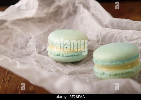 Tender green macaroons with pistachio flavor filling on paper, wooden background. Copy space. Close up shot Stock Photo