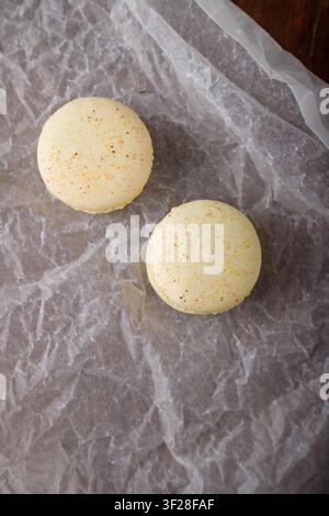 tender yellow macaroons with buttercream, salted caramel or condensed milk on paper, wooden background. Copy space, top view Stock Photo