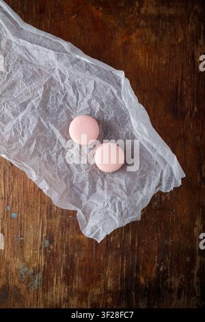 Tender pink macaroons on paper, wooden background. Forest berries, strawberry or raspberry flavor. Top view, copy space. Stock Photo