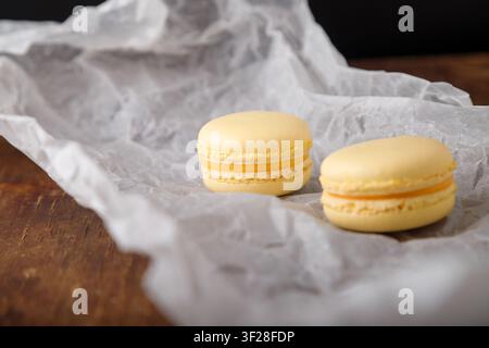 tender yellow macaroons on paper, wooden background. Fruit flavor. Mango, peach or pineapple taste. Copy space Stock Photo