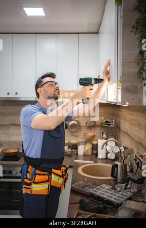 Handyman using cordless screwdriver while installing kitchen cabinets Stock Photo